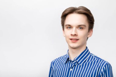 Portrait of happy cheerful young man wearing blue-white striped button shirt looking at camera smiling. Studio shot on gray background