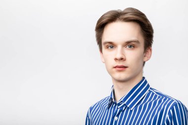 Portrait of confident teenager boy wearing blue-white striped button shirt looking at camera. Studio shot on gray background