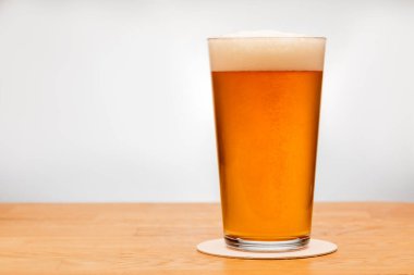 Full shaker pint glass of amber ale or beer on wooden table with grey background