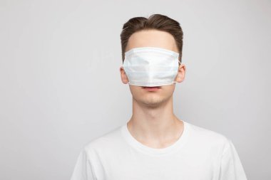 Portrait of young man wearing protective medical mask on his face covering eyes. Studio shot on gray background. Hiding from pandemic outbreak concept