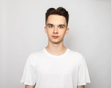 Portrait of young handsome man wearing white tshirt standing looking at camera. Studio shot on gray background