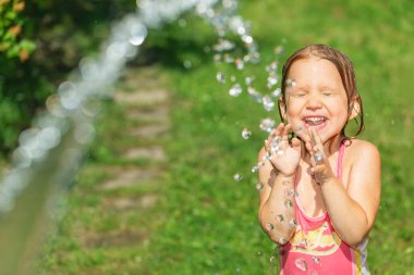 Mutlu küçük kız mayo giyip sıcak bir yaz gününde bahçe hortumuyla eğleniyor.