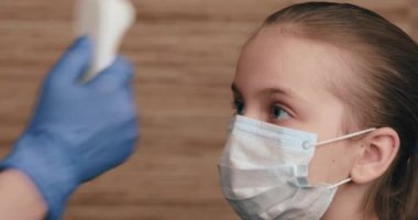 Küçük kızın vücut ısısını ölçmek için kızılötesi alın termometresi (termometre) kullanan çocuk doktoru - virüs belirtileri konseptini tarıyor