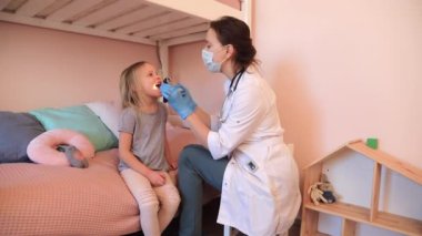 Pediyatrist Coronavirus kilitlenmesi sırasında küçük kızın boğazını kontrol ediyor.