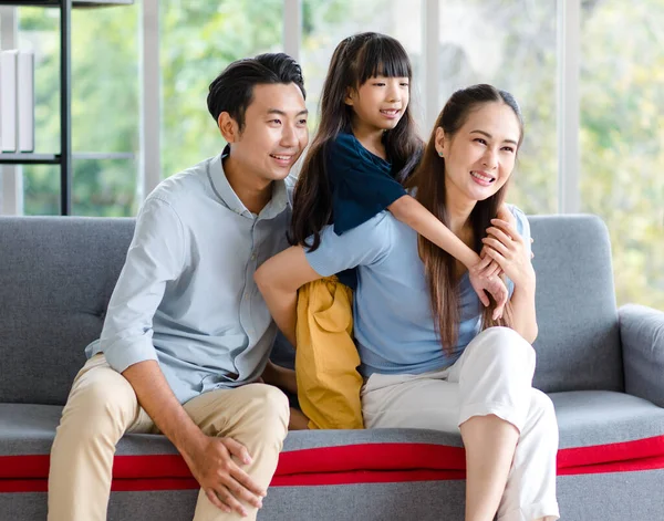 Millennial Asian happy family father mother and little young child girl sitting smiling looking at camera together on cozy sofa couch in living room home.