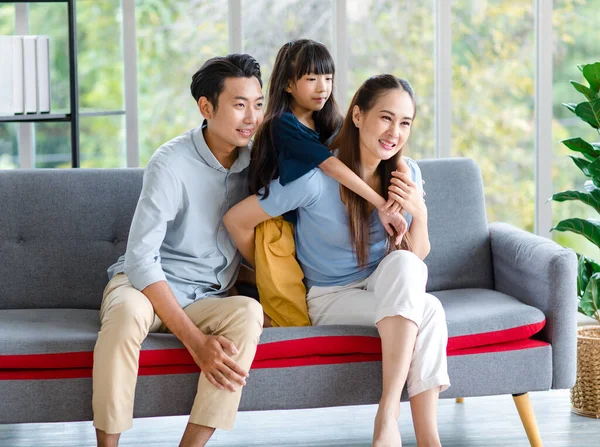 Millennial Asian happy family father mother and little young child girl sitting smiling looking at camera together on cozy sofa couch in living room home.
