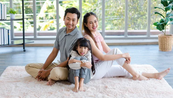 stock image Millennial Asian happy family father mother and little girl daughter in casual outfit sitting laying lying down on fluffy carpet floor smiling posing together taking photograph in living room at home.