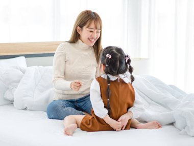 Milenyum Asyalı genç bayan genç kız anne gündelik süveter ve kot pantolon giymiş bebek bakıcısı yatak odasında küçük tatlı anaokulu kızıyla oynuyor..