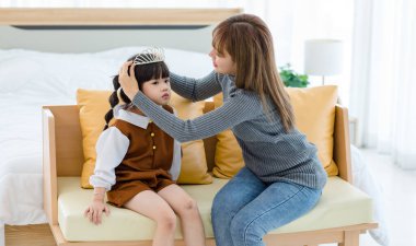 Millennial Asian pretty young female teenager mother nanny babysitter role playing smiling wearing diamond princess crown on happy cheerful little cute preschooler daughter girl head.