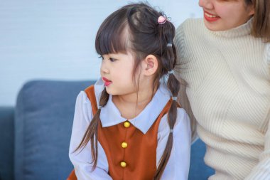 Millennial Asian happy cheerful little cute preschooler daughter girl playing learning alphabets letters jigsaw toy on sofa in living room while young teenager mother nanny helping teaching supporting