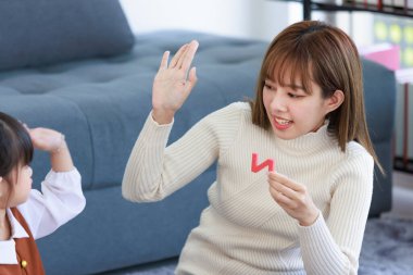 Millennial Asian happy cheerful little cute preschooler daughter girl playing learning toy on carpet floor in living room while young teenager mother nanny helping teaching supporting.