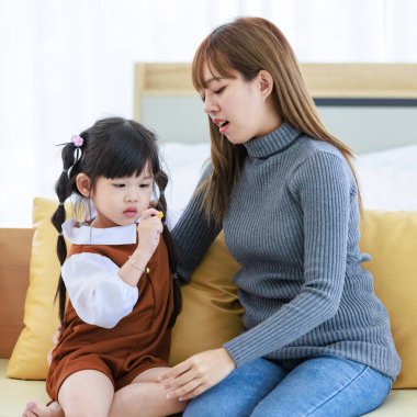 Milenyum Asyalı neşeli, mutlu, genç, güzel, genç, genç, güzel, genç, kız, anne, bebek bakıcısı, rahat koltukta oturuyor, gülümsüyor, küçük, tatlı, anaokulu kızına sevgisini gösteriyor..