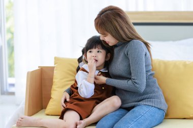 Milenyum Asyalı neşeli, mutlu, genç, güzel, genç, genç, güzel, genç, kız, anne, bebek bakıcısı, rahat koltukta oturuyor, gülümsüyor, küçük, tatlı, anaokulu kızına sevgisini gösteriyor..