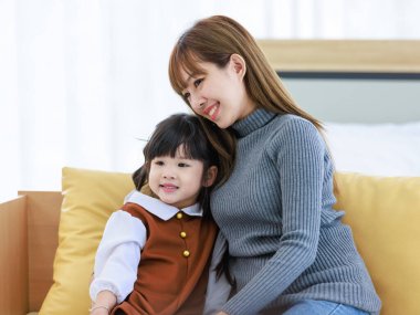 Milenyum Asyalı neşeli, mutlu, genç, güzel, genç, genç, güzel, genç, kız, anne, bebek bakıcısı, rahat koltukta oturuyor, gülümsüyor, küçük, tatlı, anaokulu kızına sevgisini gösteriyor..