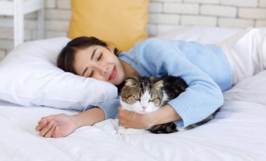 Milenyum Asyalı genç, nazik, neşe dolu kadın sahibi yatağa uzanıp sarılıyor, küçük sevimli, sevimli, evcil kedicik, tüylü kedicik evcil kedicik dostuna sevgisini gösteriyor..