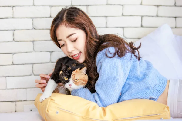 stock image Millennial Asian young kindly cheerful female owner laying lying down on pillows cozy sofa bed hugging cuddling cute little domestic kitten tricolor furry pussycat pet friend in living room at home.