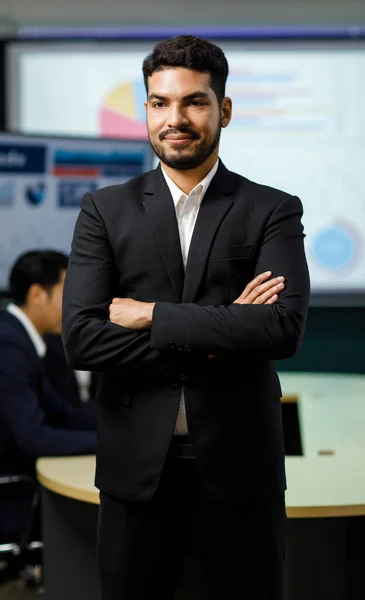 Millennial Asian Indian professional successful bearded male businessman entrepreneur ceo management in formal business suit standing smiling crossed arms portrait photo in company office meeting room