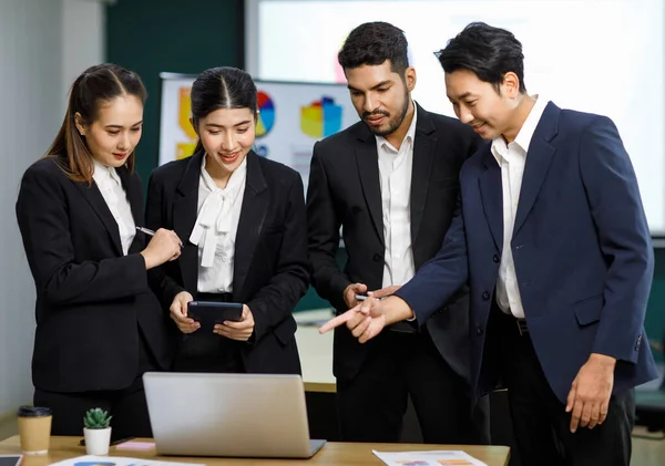 Millennial Asian Indian professional male businessmen female businesswomen employee staff colleagues in formal business suit standing discussing brainstorming working together with laptop computer.