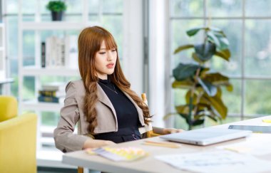 Asyalı profesyonel başarılı düşünceli genç bayan iş kadını yaratıcı grafik tasarımcı günlük moda takım elbise ceketli çözüm fikirleri içinde oturuyor..