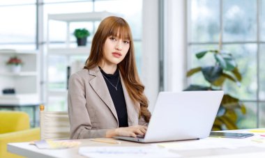 Asyalı profesyonel başarılı genç bayan iş kadını yaratıcı grafik tasarımcı günlük modaya uygun takım elbise ceket giyen ofis iş yerindeki dizüstü bilgisayarla çalışıyor..