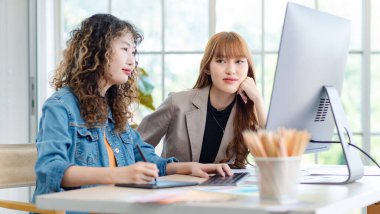 Asyalı profesyonel başarılı genç bayan yaratıcı tasarımcı gündelik kıyafetleriyle oturmuş, Stylus kalem ile çizim çizerken meslektaşı sohbet ederken ofiste mola veriyor..