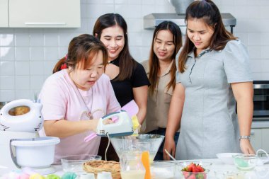 Asyalı profesyonel kadın fırın şefi elinde yumurta çırpma makinesi, cam kasede yumurta çırpma makinesi, ev hanımlarına tam donanımlı mutfakta un hamuru yapmayı öğretiyor..