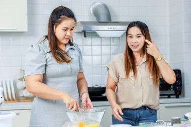 Asyalı profesyonel kadın pastane şefi ev hanımı ve arkadaşı sütçülerin taze sütü, dekore edilmiş mutfakta cam bardağa doldurup lezzetli bir tatlı pişirmeye yardım ediyorlar..