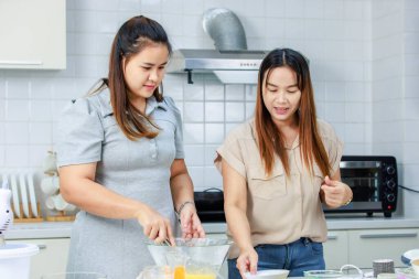 Asyalı profesyonel kadın pastane şefi ev hanımı ve arkadaşı sütçülerin taze sütü, dekore edilmiş mutfakta cam bardağa doldurup lezzetli bir tatlı pişirmeye yardım ediyorlar..