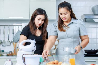 Asyalı, profesyonel kadın pastacı fırıncı aşçı ev hanımı arkadaşı gülümseyen, paslanmaz elek ile cam kâseye un karıştıran, dekore edilmiş mutfakta hamur hazırlayan.