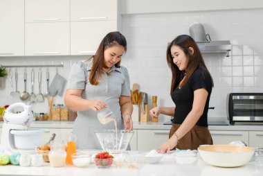 Asyalı, profesyonel kadın pastacı fırıncı aşçı ev hanımı arkadaşı gülümseyen, paslanmaz elek ile cam kâseye un karıştıran, dekore edilmiş mutfakta hamur hazırlayan.