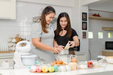 Asyalı, profesyonel kadın pastacı fırıncı aşçı ev hanımı arkadaşı gülümseyen, paslanmaz elek ile cam kâseye un karıştıran, dekore edilmiş mutfakta hamur hazırlayan.