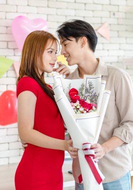 Asyalı genç, yakışıklı erkek arkadaş sevgililer gününde romantik dekore edilmiş oturma odasında çiçek buketi ile evlenme teklifi yüzüğü veriyor..