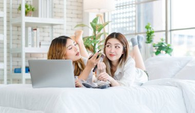 İki mutlu Asyalı güzel bayan kozmetik, cilt güzellik ürünlerine yüz bakımı yapar, dizüstü bilgisayar seyreden kadın, beyaz bir yatakta dinlenir, ergen ya da evdeki arkadaş yaşam tarzını kavrar..