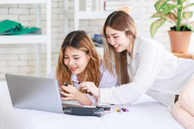 İki mutlu Asyalı güzel bayan kozmetik, cilt güzellik ürünlerine yüz bakımı yapar, dizüstü bilgisayar seyreden kadın, beyaz bir yatakta dinlenir, ergen ya da evdeki arkadaş yaşam tarzını kavrar..