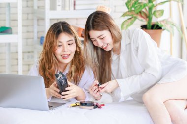 İki mutlu Asyalı güzel bayan kozmetik, cilt güzellik ürünlerine yüz bakımı yapar, dizüstü bilgisayar seyreden kadın, beyaz bir yatakta dinlenir, ergen ya da evdeki arkadaş yaşam tarzını kavrar..