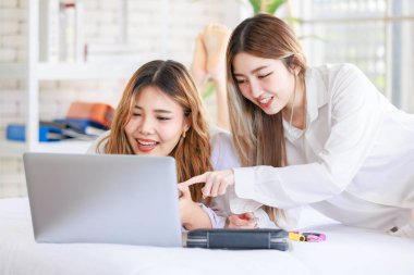 İki mutlu Asyalı güzel bayan kozmetik, cilt güzellik ürünlerine yüz bakımı yapar, dizüstü bilgisayar seyreden kadın, beyaz bir yatakta dinlenir, ergen ya da evdeki arkadaş yaşam tarzını kavrar..