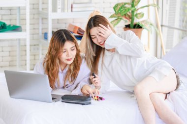 İki mutlu Asyalı güzel bayan kozmetik, cilt güzellik ürünlerine yüz bakımı yapar, dizüstü bilgisayar seyreden kadın, beyaz bir yatakta dinlenir, ergen ya da evdeki arkadaş yaşam tarzını kavrar..