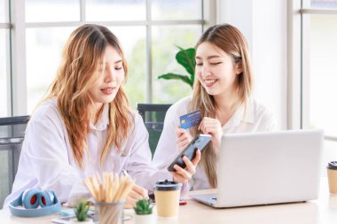 İki mutlu kadın, bilgisayarını kullanan güzel bir Asyalı kadın online alışveriş yaparken gülümseyen bir bilgisayar ve oturma odasında bir kredi kartı. Genç ya da arkadaş kavramı, evde birlikte zaman geçirmek..
