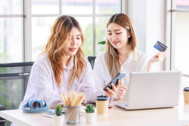 İki mutlu kadın, bilgisayarını kullanan güzel bir Asyalı kadın online alışveriş yaparken gülümseyen bir bilgisayar ve oturma odasında bir kredi kartı. Genç ya da arkadaş kavramı, evde birlikte zaman geçirmek..