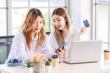 İki mutlu kadın, bilgisayarını kullanan güzel bir Asyalı kadın online alışveriş yaparken gülümseyen bir bilgisayar ve oturma odasında bir kredi kartı. Genç ya da arkadaş kavramı, evde birlikte zaman geçirmek..