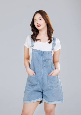 Asyalı sevimli, neşeli, kot pantolon giyen genç bir kızın portresi mutlu ve tatlı gülüşlü, beyaz arka planda soyutlanmış bir şekilde duran şık model bir kadın, gençlik ve gençlik modası.