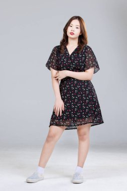 Asyalı, sevimli, neşeli, küçük çiçek desenli bir elbise giyen genç kızın portresi. Siyah elbise, şık model bir kadın. Mutlu ve hoş bir gülümseme.