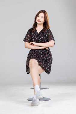 Asyalı, sevimli, neşeli, küçük çiçek desenli bir elbise giyen genç kızın portresi. Siyah elbise, şık model bir kadın. Mutlu bir gülümseme..