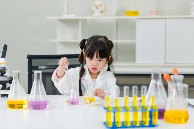 Laboratuvar önlüğü giymiş Asyalı küçük şirin kız öğrenciler deney tüpü bilim deneyleri yapıyorlar. Okulda kimya laboratuvarında. Eğitim araştırma ve geliştirme kavramı çocukları eğitiyor.