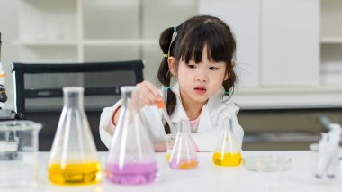 Laboratuvar önlüğü giymiş Asyalı küçük şirin kız öğrenciler deney tüpü bilim deneyleri yapıyorlar. Okulda kimya laboratuvarında. Eğitim araştırma ve geliştirme kavramı çocukları eğitiyor.