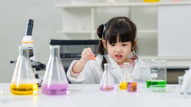 Laboratuvar önlüğü giymiş Asyalı küçük şirin kız öğrenciler deney tüpü bilim deneyleri yapıyorlar. Okulda kimya laboratuvarında. Eğitim araştırma ve geliştirme kavramı çocukları eğitiyor.