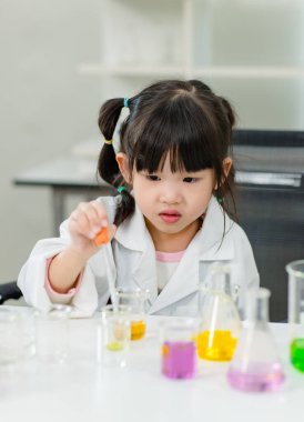 Laboratuvar önlüğü giymiş Asyalı küçük şirin kız öğrenciler deney tüpü bilim deneyleri yapıyorlar. Okulda kimya laboratuvarında. Eğitim araştırma ve geliştirme kavramı çocukları eğitiyor.
