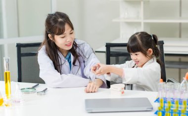 Beyaz önlüklü Asyalı cesur küçük kız klinikte çalışırken gülümseyen güzel kadın doktorun koluna aşı enjekte ediyor. Eğitim sağlık tıbbı çocuklar için hastane kavramını öğreniyor