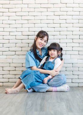 Mutlu Asyalı genç anne ve tatlı kız gülümseyen küçük kız beyaz tuğla duvar arkasında poz veren stüdyo resmi Anneler Günü aile babalığı kavramını seviyor..