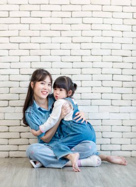 Mutlu Asyalı genç anne ve tatlı kız gülümseyen küçük kız beyaz tuğla duvar arkasında poz veren stüdyo resmi Anneler Günü aile babalığı kavramını seviyor..